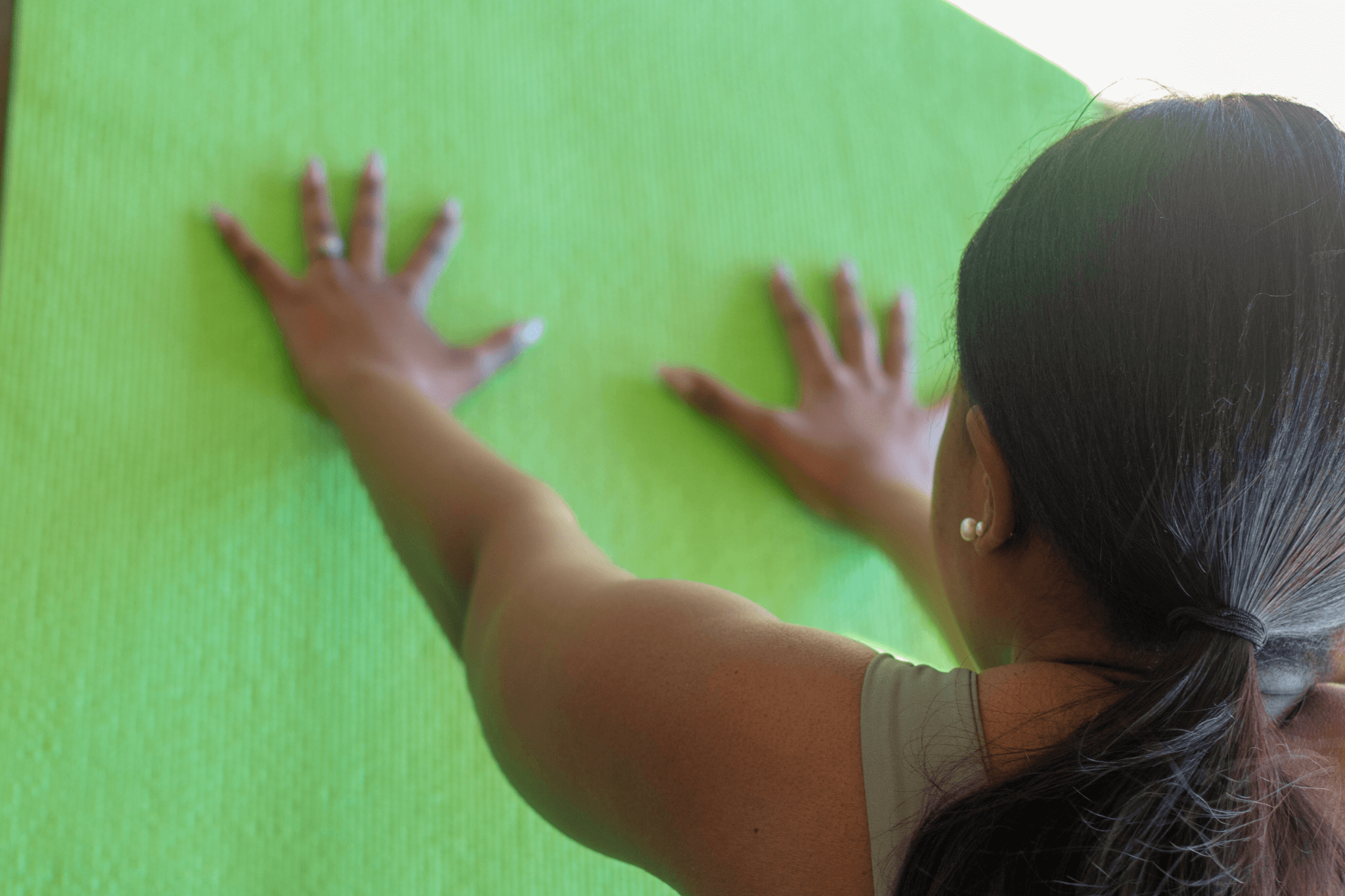 Woman placing her hands on a green yoga mat while preparing for a yoga practice.
