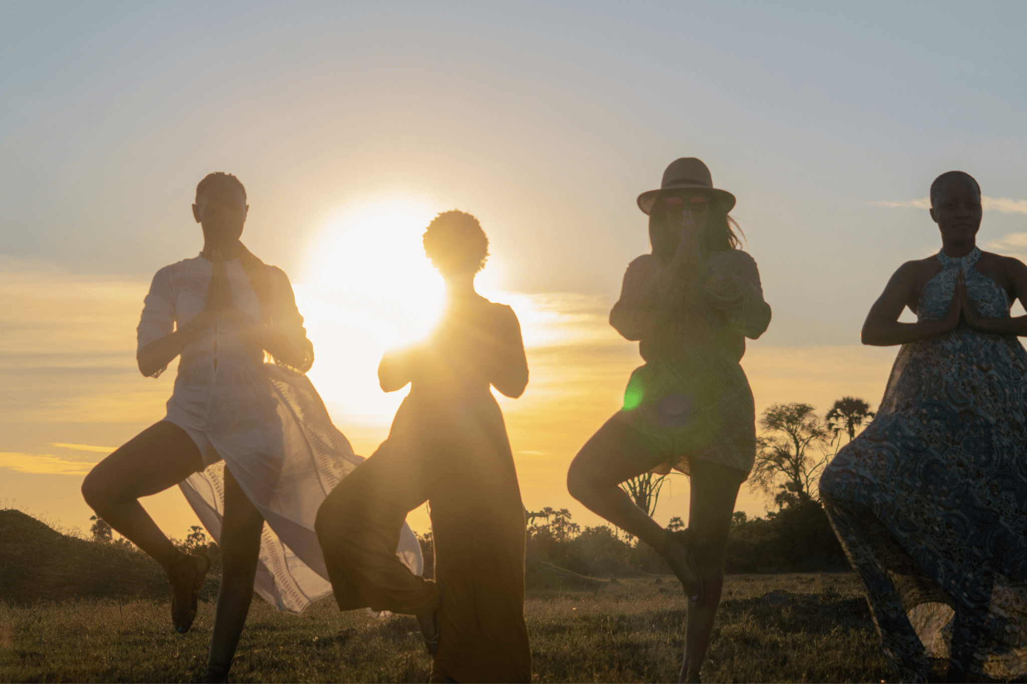 Group of women holding a yoga balance pose together at sunset during a yoga safari retreat.